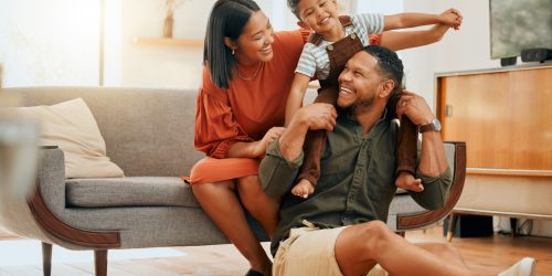 A happy mixed race family of three relaxing in the lounge and being playful together. Loving black family bonding with their son while playing fun games on the sofa at home
