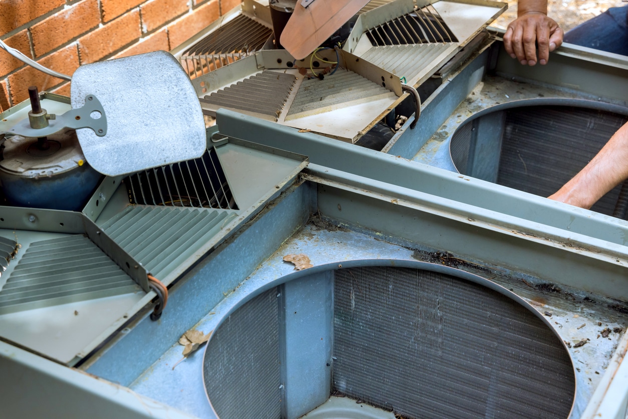 Technician performing HVAC upgrades during routine maintenance on an outdoor AC unit at a residential property.