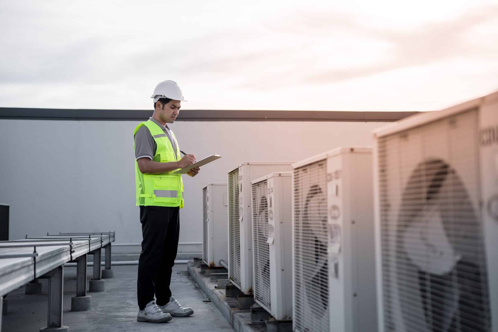 Inspector checking the energy efficiency of commercial HVAC system on roof of building.
